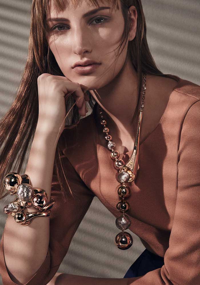 GRAZIELLA LUXURY From the Universe collection: necklace and bangles in 18kt yellow gold with inserts in rose and white gold. Created using gloss and satin electroforming. Chiseled engraved decorative details.   Sweater Wolford, skirt Gaetano Navarra 