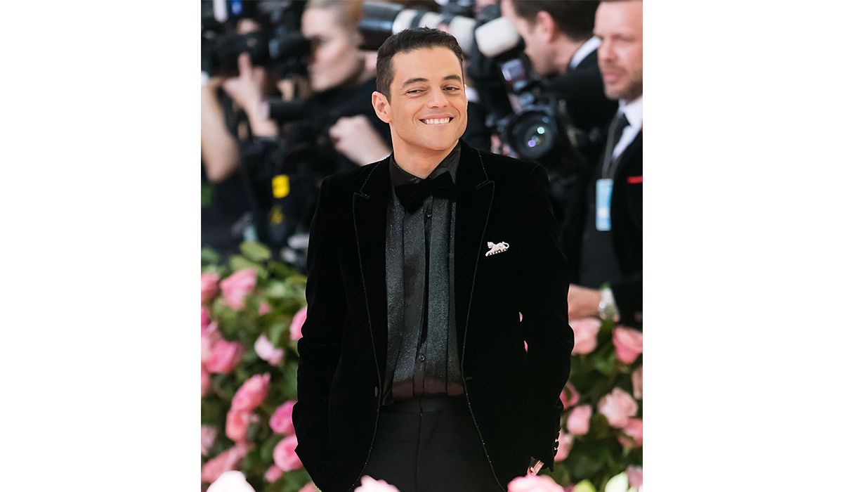 Rami Malek wearing a Panthère de Cartier brooch, and a Cartier Tank MC watch